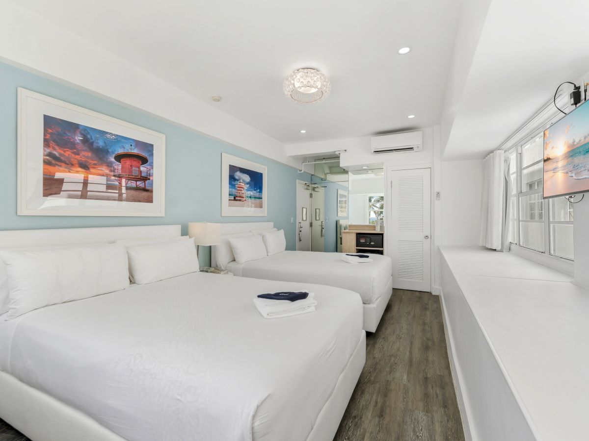A bright hotel room with two beds, wall art, a TV, and wooden floors, blending modern decor with comfort in a serene atmosphere.