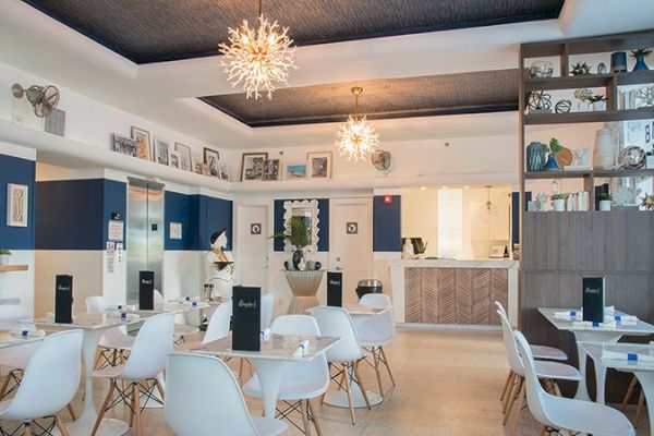 A modern café or restaurant with white chairs, tables, decorative lights, wall art, and a wooden shelving unit adorned with various items.