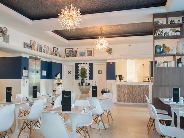 A modern café or restaurant with white chairs, tables, decorative lights, wall art, and a wooden shelving unit adorned with various items.