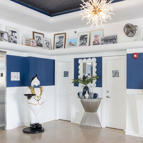 A stylish reception area with blue and white decor, featuring an elevator, decorative figurine, framed pictures, and a reception desk.