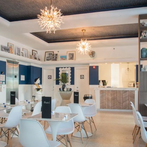 This image shows a modern, stylish dining area with white furniture, decorative lighting, and neatly arranged blue menus on the tables, ending the sentence.