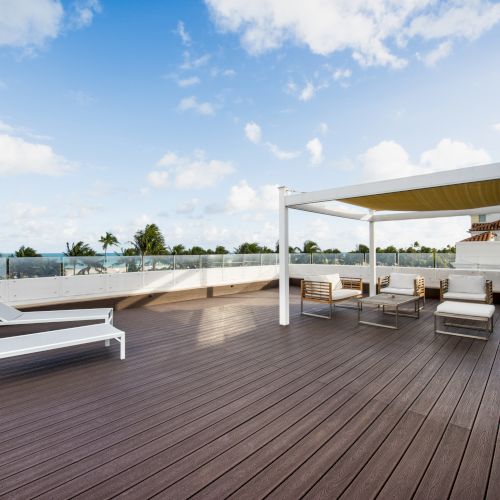 A spacious rooftop deck with lounge chairs, a pergola with seating underneath, and scenic views of palm trees and blue skies in the background.