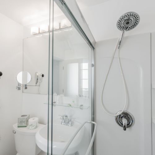 This image shows a clean, modern bathroom with a glass shower, wall-mounted hair dryer, sink, toilet, and various toiletries arranged neatly.